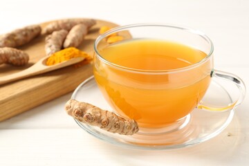 Aromatic turmeric tea in glass cup, roots and powder on white wooden table, closeup