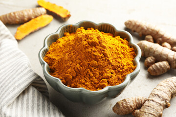 Aromatic turmeric powder in bowl and fresh roots on light grey table, closeup