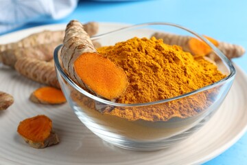 Aromatic turmeric powder in bowl and fresh roots on light blue table, closeup
