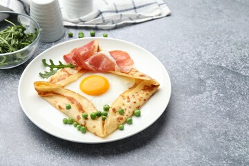 Delicious crepe with egg, bacon, arugula and green peas on grey table, closeup. Space for text