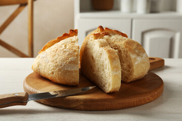 Cut freshly baked bread and knife on white wooden table, closeup