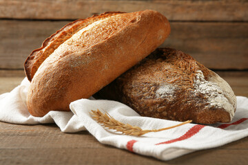 Loaves of freshly baked bread and spike on wooden table, closeup