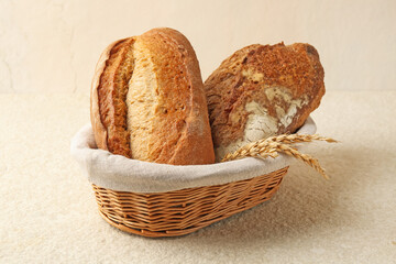Different types of fresh bread and spikelets in wicker basket on light textured table, closeup