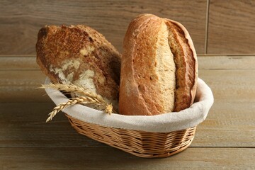 Different types of fresh bread and spikelets in wicker basket on wooden table, closeup