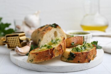Tasty bread with garlic, herbs and oil on white tiled table, closeup