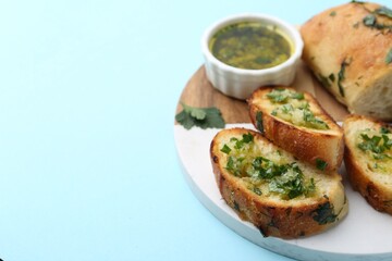 Tasty bread with garlic, herbs and oil on light blue background, closeup. Space for text