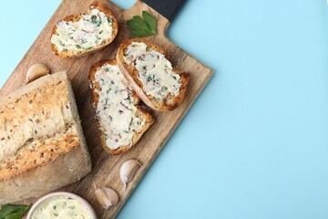 Tasty bread with garlic, herbs and butter on light blue background, top view. Space for text