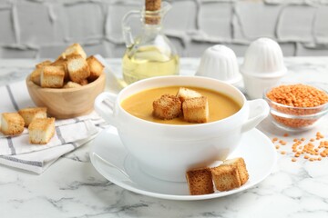 Delicious lentil cream soup served with croutons on white marble table