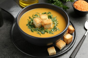 Delicious lentil cream soup served with croutons on grey table, closeup