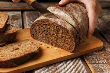 Woman cutting fresh bread at wooden table, closeup