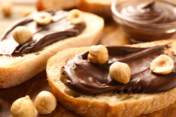 Slices of bread with chocolate spread and hazelnuts on wooden table, closeup