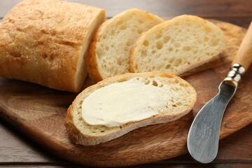 Piece of bread with butter and knife on wooden table, closeup