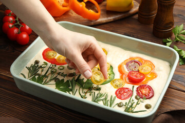 Woman adding tomato to raw focaccia at wooden table, closeup