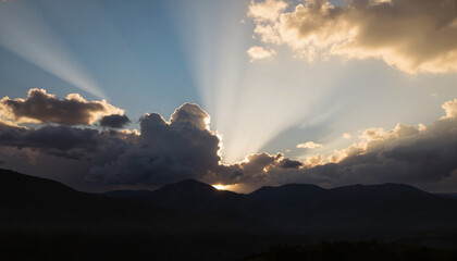 Sun rays breaking through storm clouds over mountains, dramatic scenery