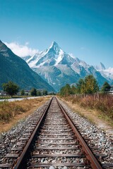Fototapeta premium Railway leading through scenic valley with snow-covered mountains and clear blue sky in bright daylight