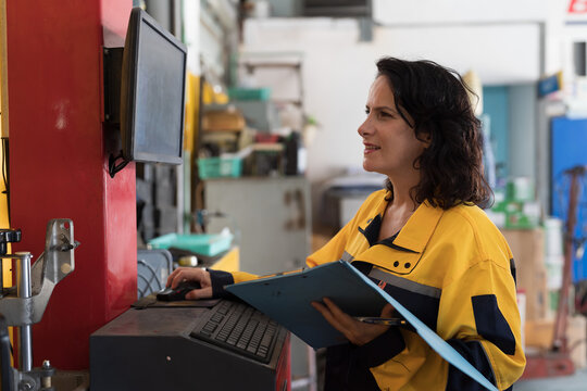 Woman worker wearing safety uniform work in the industry factory, control and monitor CNC machine. Factory worker maintaining machine on monitor in the industrial factory