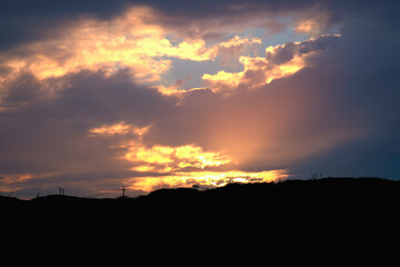 A stunning sunset captured over the rolling hills in Shimen, New Taipei City, Taiwan, with the sky painted in vivid hues of orange, yellow, and blue.