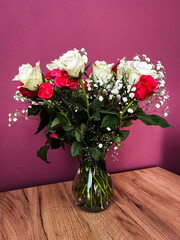 Bouquet of roses in a transparent vase on a wooden table against a purple wall background