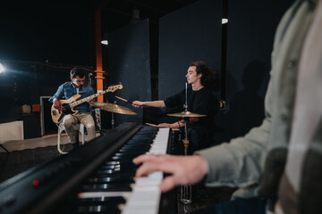A music band practices together in a studio. Instruments include a bass guitar, piano, and drums.