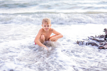 Boy playing with waves while squatting on sandy beach at sunset