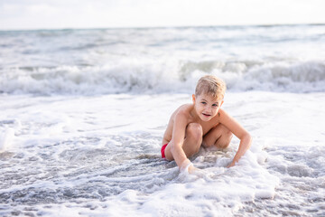 Boy playing with waves while squatting on sandy beach at sunset