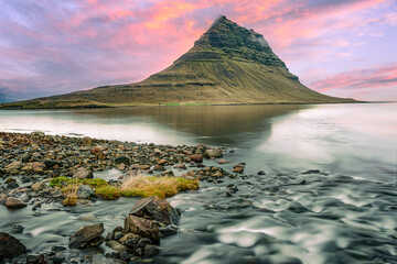 Kirkjufell mountain, Iceland, stands majestically above tranquil waters, its serene reflection...