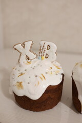 Easter cake with white glaze, decorated with almond petals, silver beads, and flowers, topped with cookies shaped as 