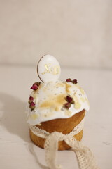 Easter cake with white glaze, decorated with almond petals, silver beads, and flowers, topped with cookies shaped as 