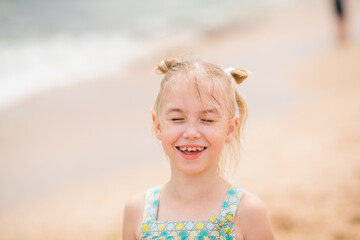 Close-up portrait of a smiling girl with pigtails and windblown hair on a cloudy beach day
