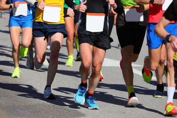 Muscular legs of runners in competition in the city road race with unrecognizable faces ideal as a...