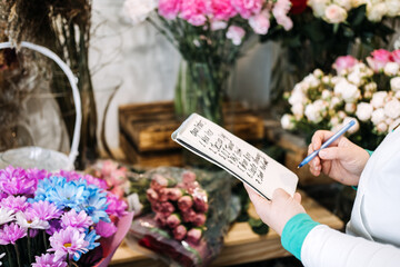 Florist writing down open bouquet orders in a notepad while surrounded by vibrant floral...