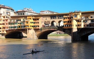 Fototapeta premium Famous bridge called PONTE VECCHIO in italian city of FLORENCE and Arno River with blue sky and a canoe