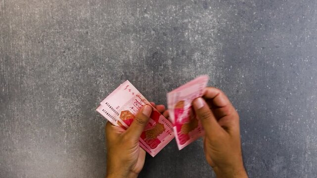 close-up of a man hands holding and counting one hundred rupees banknotes of Pakistan.