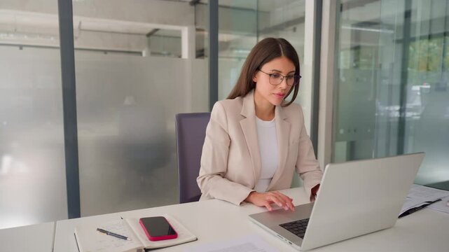 Focused middle aged business woman using laptop at work in office. Professional female executive entrepreneur in suit working on computer pc at company workplace, doing financial analyze. Copy space