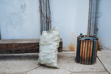 A bag filled with garbage is currently sitting right next to a wooden trash can, which provides an...