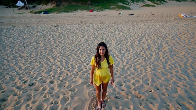 beauty woman in her early 20s with long hair wearing a wet yellow t-shirt looking at camera on a beach in summer during her holidays vacation
