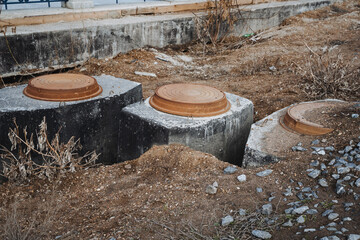 A group of concrete septic tanks is sitting in the dirt, waiting for installation. These tanks...