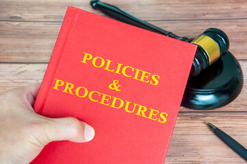Hand holding Policies and Procedures book with gavel on a wooden table background