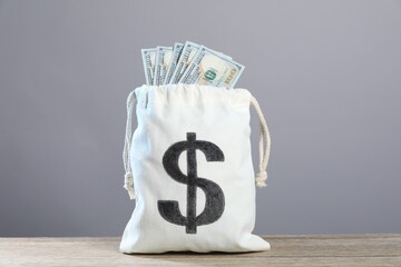 Dollar banknotes in burlap sack on wooden table against grey background