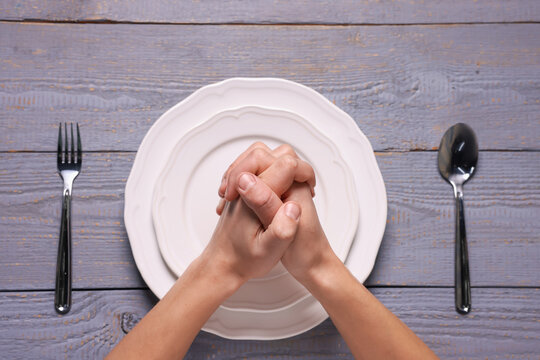 Man praying before eating at grey wooden table with plate and cutlery, top view