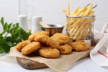 Tasty chicken nuggets, potato fries and sauce on white tiled table, closeup