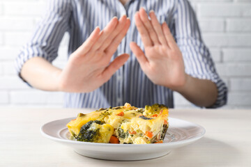 Woman refusing to eat piece of casserole at table, closeup