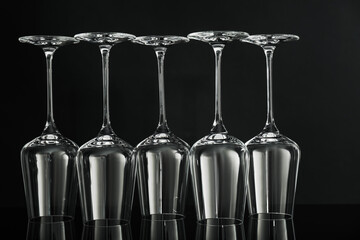 Many empty clean glasses on mirror surface against black background
