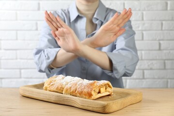Woman refusing to eat apple strudel at wooden table near white brick wall, selective focus. Food allergy concept