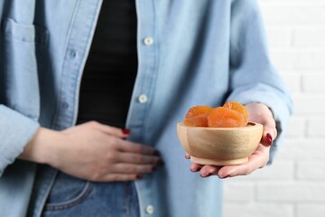 Woman refusing to eat dried apricots near white brick wall, closeup. Food allergy concept