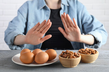 Woman refusing to eat products at grey wooden table, selective focus. Food allergy concept