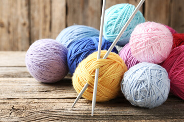 Balls of colorful yarn and knitting needles on wooden table, closeup