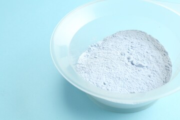 Bowl with hair bleaching powder on light blue background, closeup