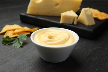 Tasty dipping cheese sauce in bowl, nacho chips and parsley on black table, closeup