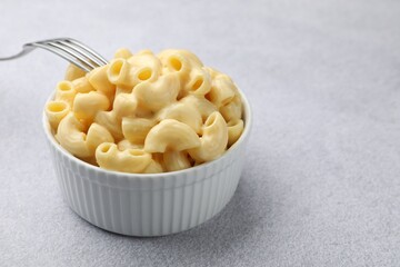 Delicious pasta with cheese sauce in bowl and fork on grey table, closeup. Space for text
